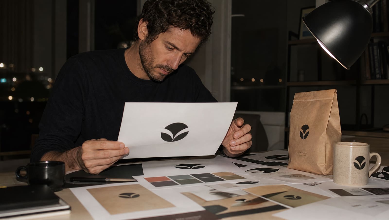 Mesa de diseñador con bocetos de logotipo, muestras de color y tarjetas impresas de una marca en distintas versiones