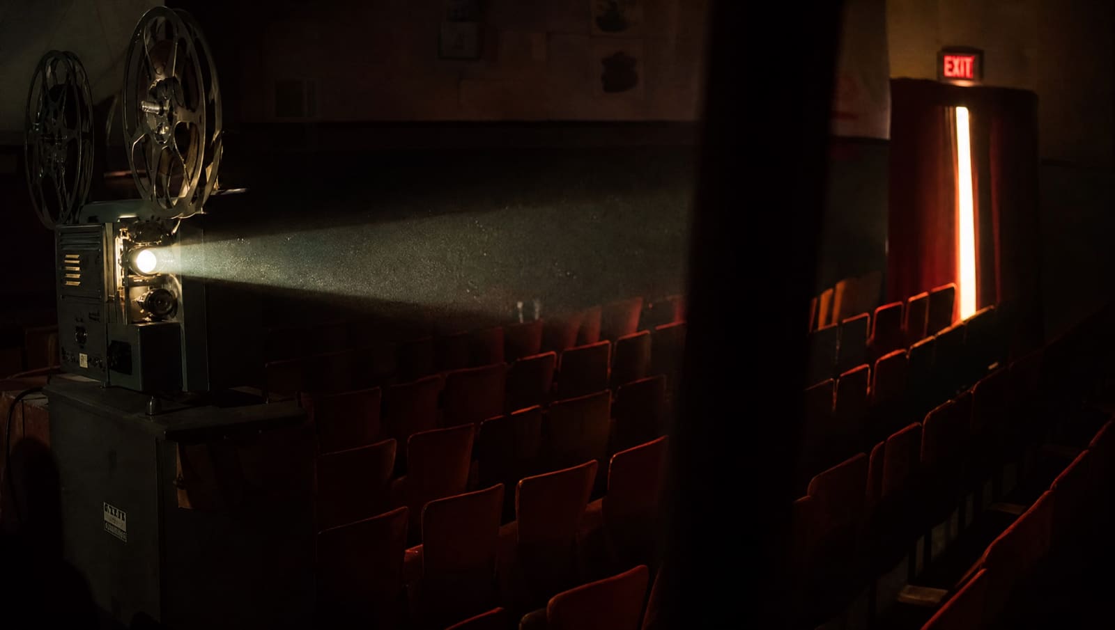 Un proyector de cine antiguo se apaga en una sala vacía y su último haz de luz se deshace en el polvo sobre las butacas rojas